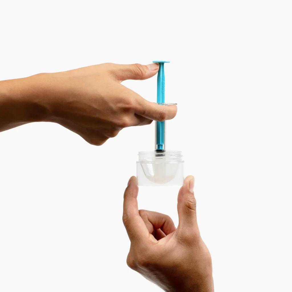 hands using a blue syringe to extract contents from a clear container for a home insemination kit